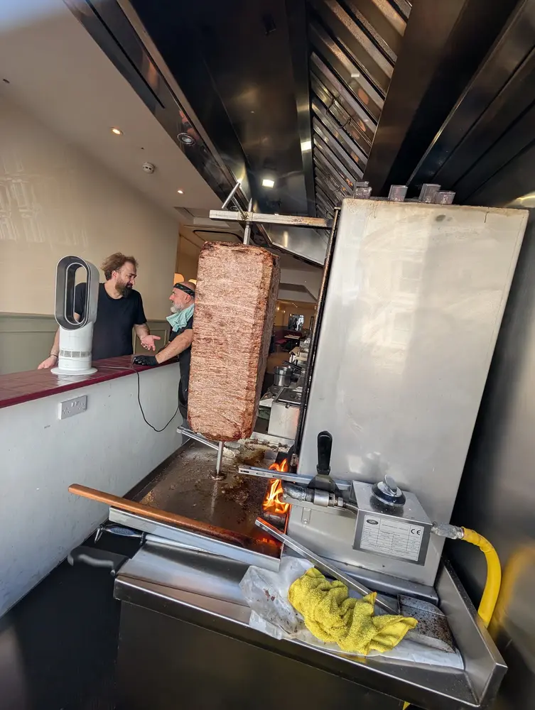 Two members of the team beside the veal döner turning over the open fire in the kitchen